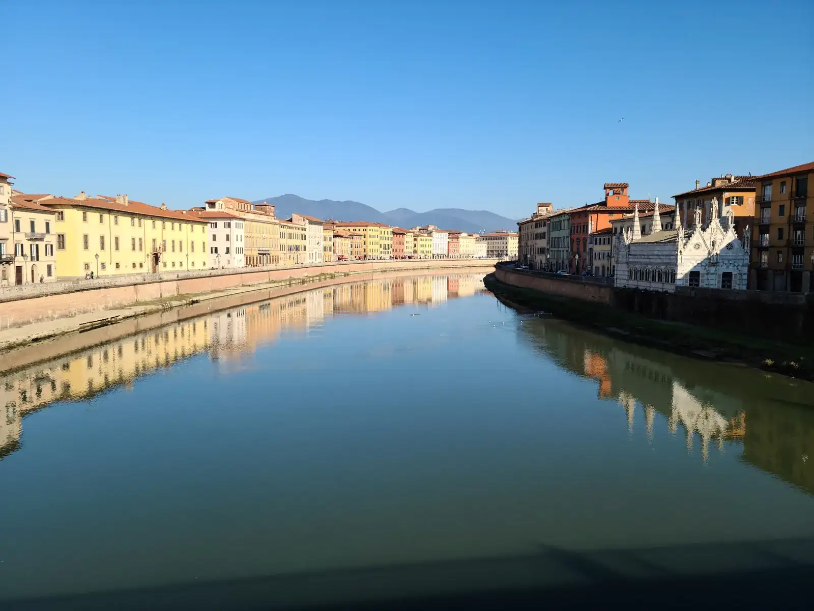 The Arno River in Pisa with the Gothic church of Santa Maria della Spina on the bank and mountains visible in the distance