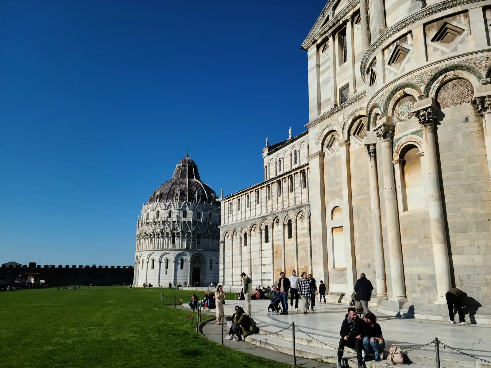 The Baptistery of San Giovanni and Cathedral of Santa Maria Assunta seen from across the green lawn of Piazza dei Miracoli