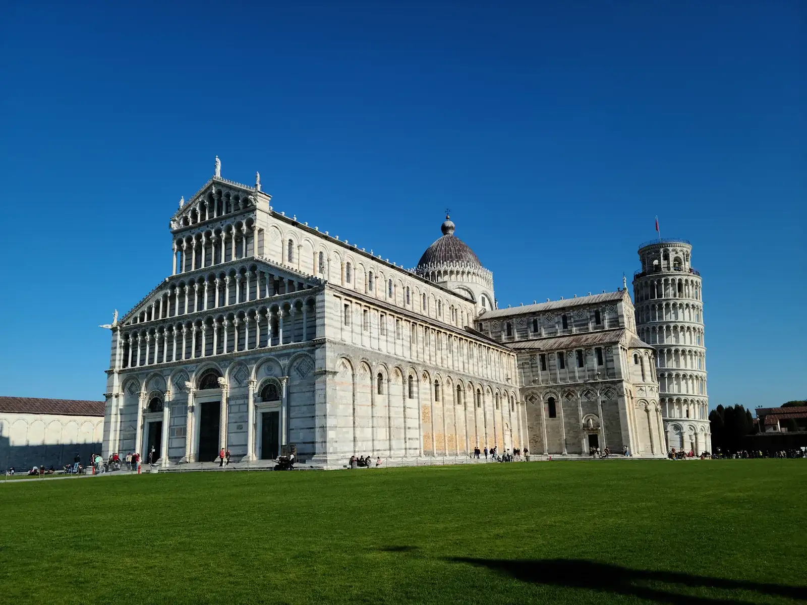 The white marble facade of the Cathedral of Santa Maria Assunta with the Leaning Tower visible behind it against a clear blue sky