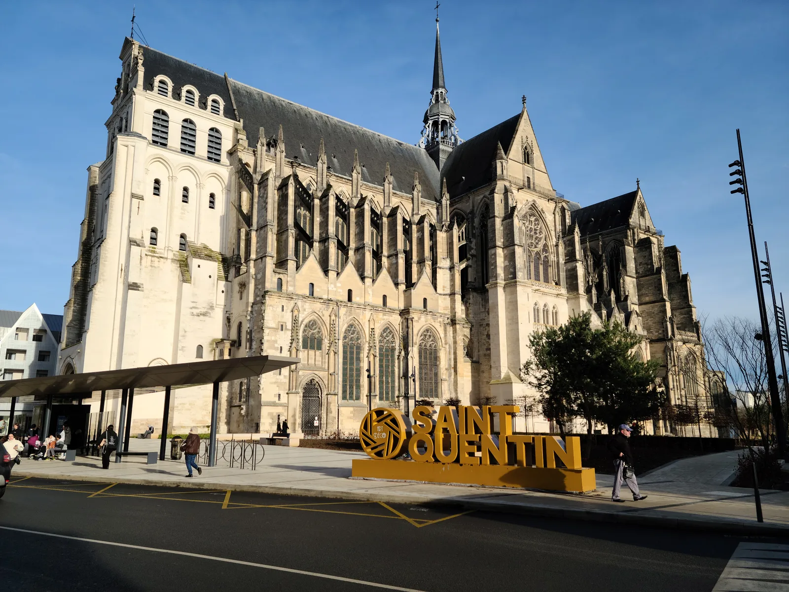 Basilique de Saint-Quentin by day with a gold painted informational sign in the foreground