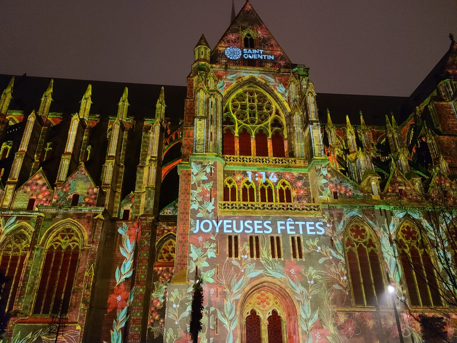 Joyeuses Fêtes holiday message projected in light onto the Basilique de Saint-Quentin facade