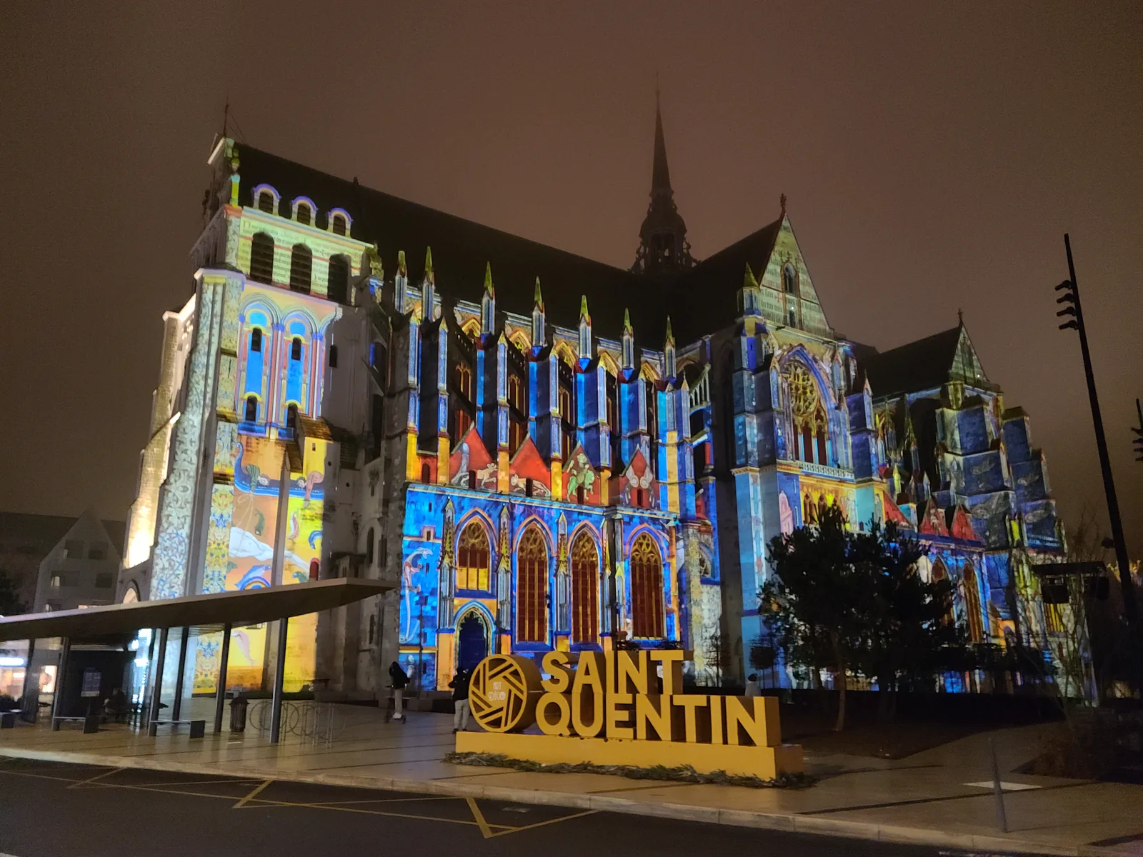 Basilique de Saint-Quentin light show with a decorative sign in the foreground at night