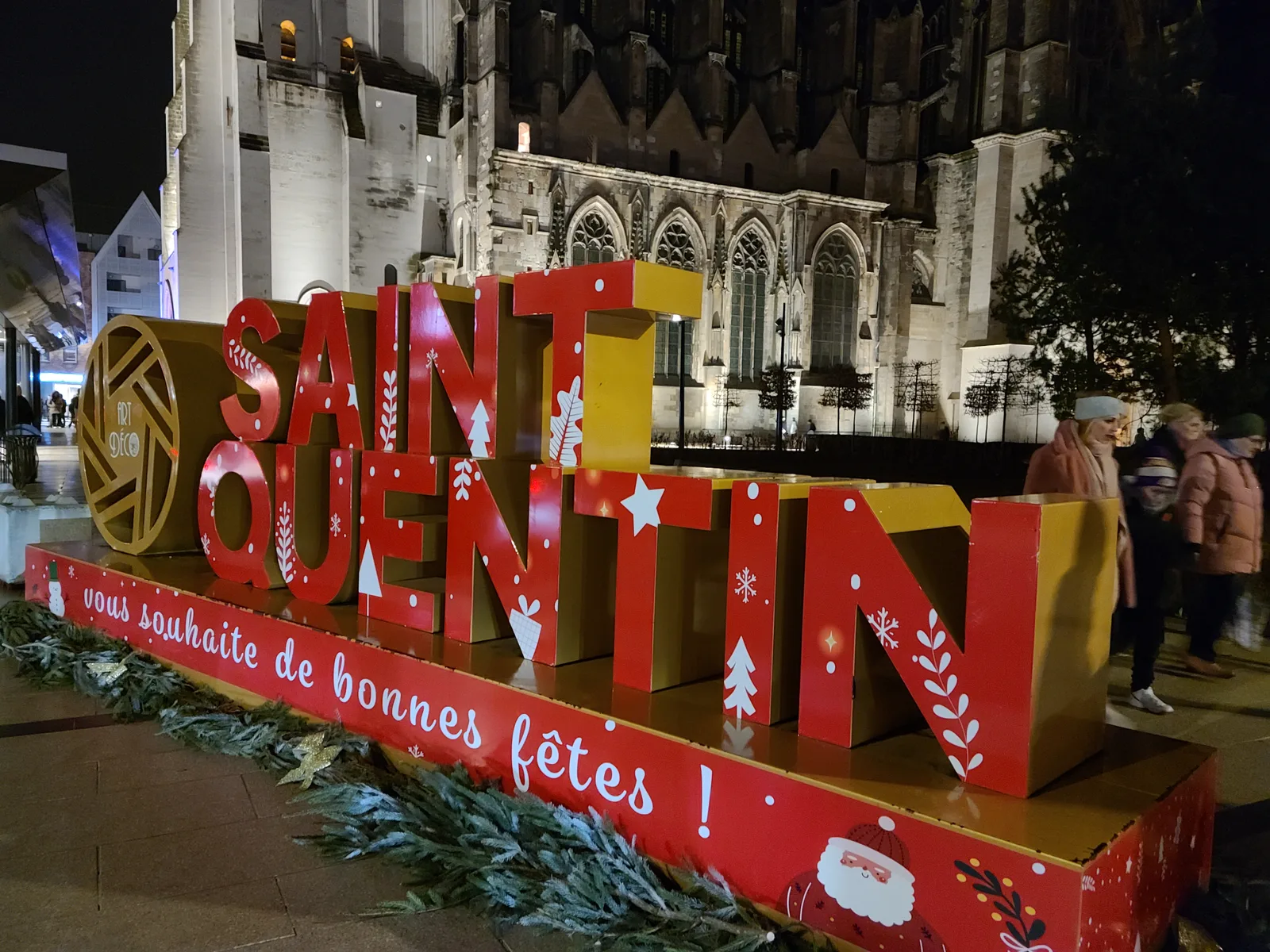 Christmas sign in front of the illuminated Basilique de Saint-Quentin at night